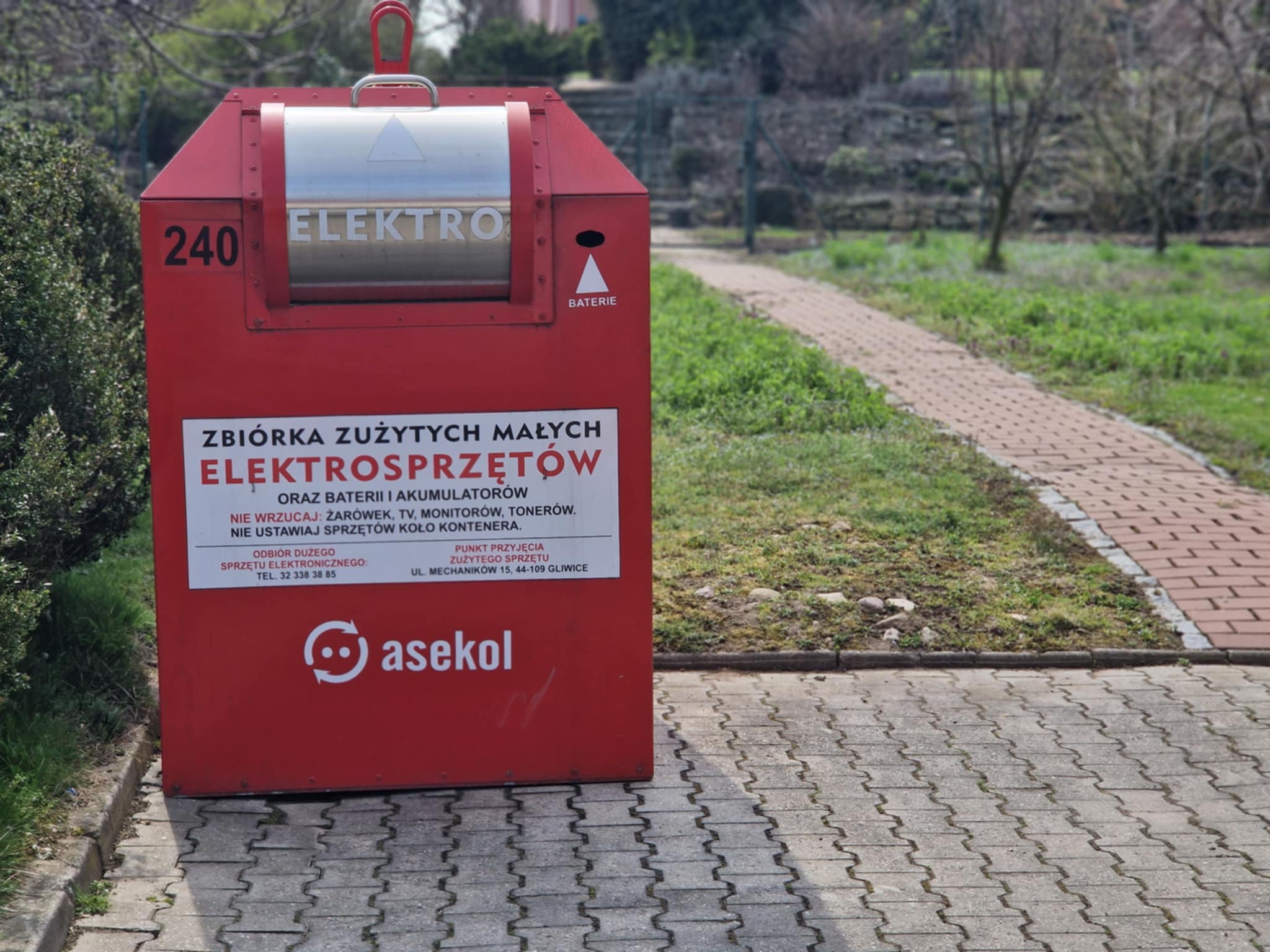 Zdjęcie czerwonego pojemnika na elektroodpady znajdującego się w Przewornie przy parkingu Zakładu Usług Komunalnych.